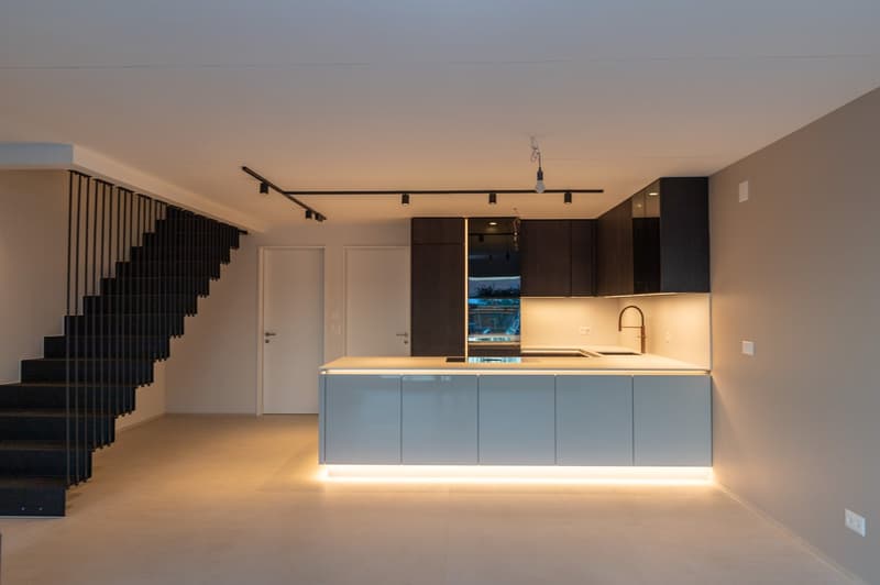 Modern kitchen with open floor plan, sleek black metal staircase, white countertops, integrated sink, and recessed lighting.