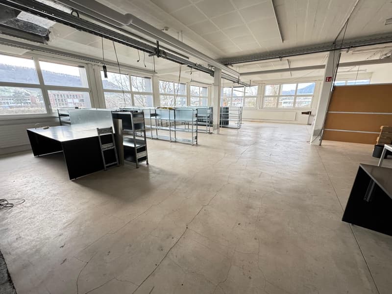 Large open commercial space with concrete flooring, metal shelving units, and large windows providing natural light. The space appears to be an industrial or warehouse-style setting, potentially suitable for a variety of commercial uses.