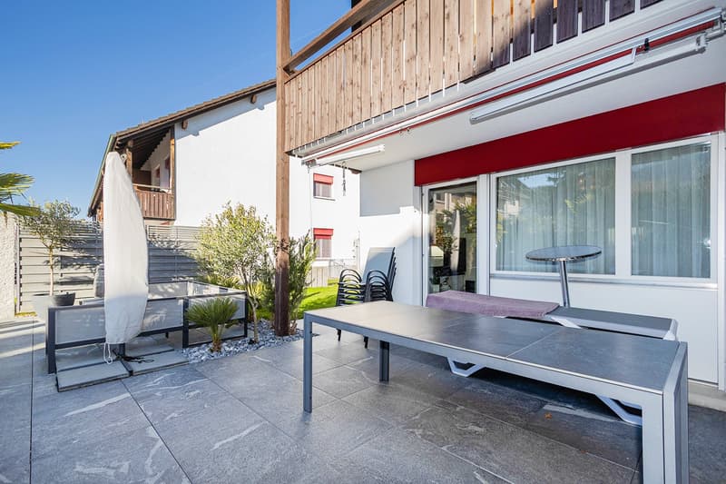 Patio area with table, chairs, loungers, potted plants, and a closed umbrella.