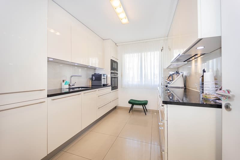 Modern kitchen, black countertops, stainless steel appliances, white cabinetry, tiled flooring