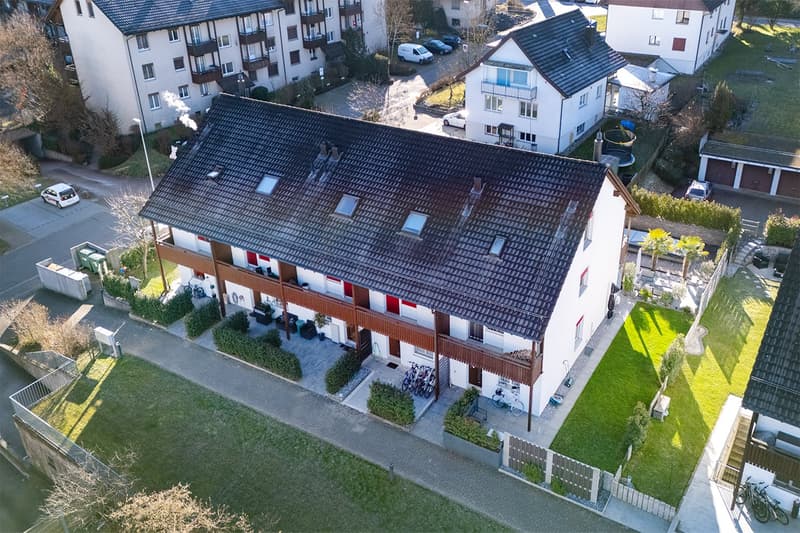White 2-story house, brown roof, large windows, balcony on the second floor, bikes parked in front