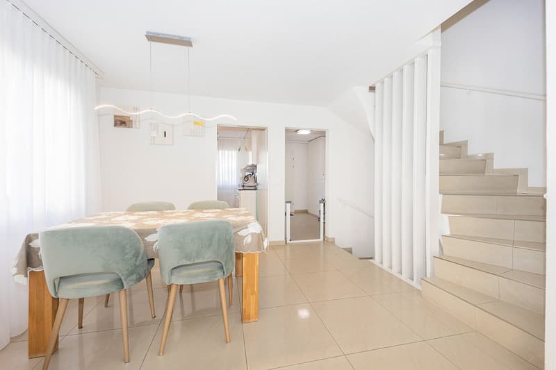Dining area with wooden table, dining chairs, stairs, open kitchen, white walls, modern ceiling lights