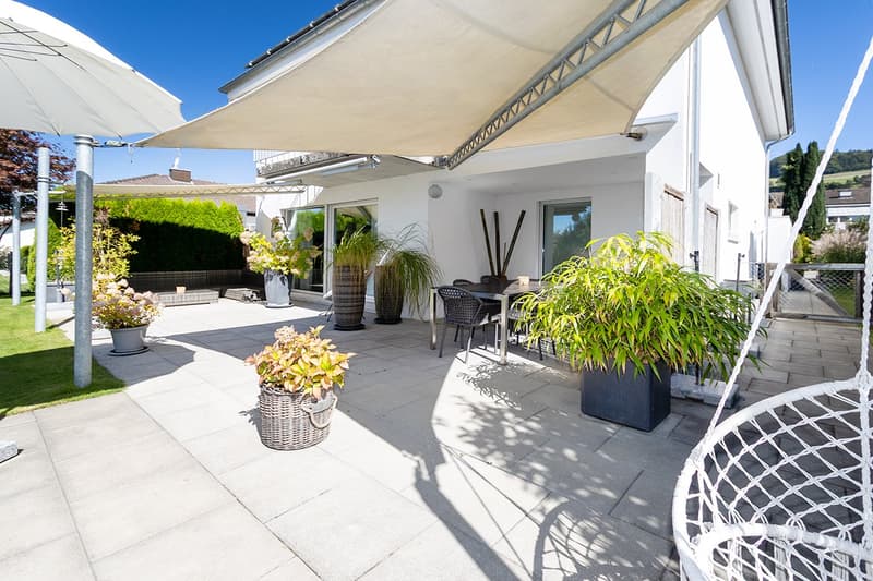 Tiled patio, shade sail, outdoor dining table, wicker chairs, plants in pots, outdoor hanging swing