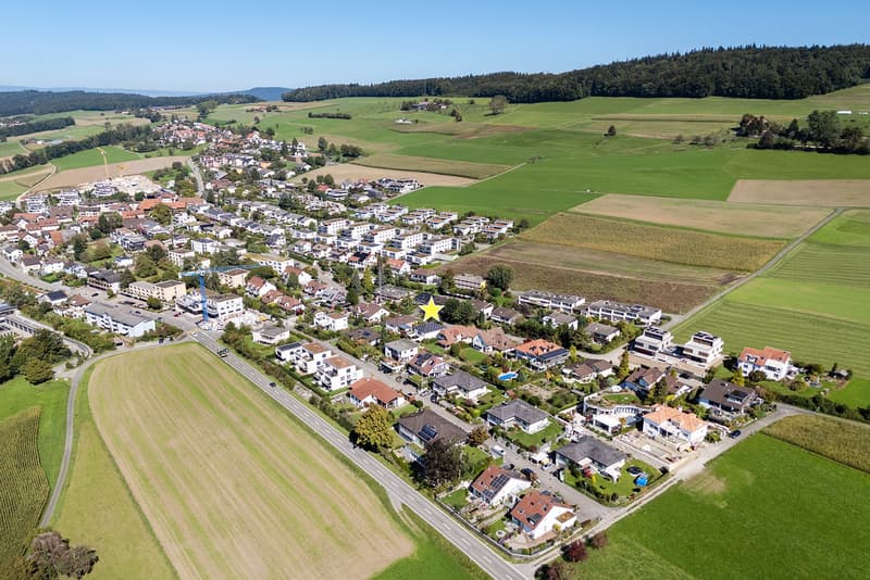 Suburban area with many detached and semi-detached houses, green fields, and a clear view of the surrounding landscape