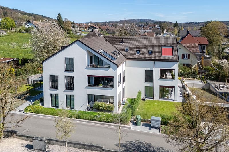 2 story house, white exterior, brown roof, multiple windows, balconies, solar panels, garden, driveway