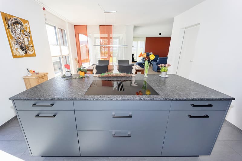 modern kitchen with granite countertop, island stove, gray cabinets, dining table, flowers, painting