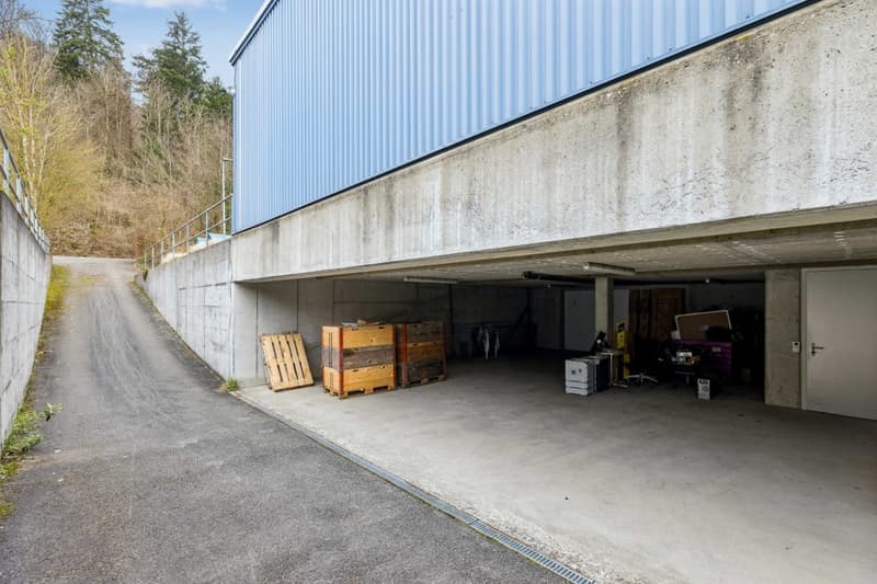 Underground parking area with concrete walls, blue metal siding, wooden pallets, and various items inside