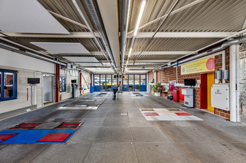 Empty garage with metal grates on the floor, brick walls, metal pipes, and monitors on the wall.