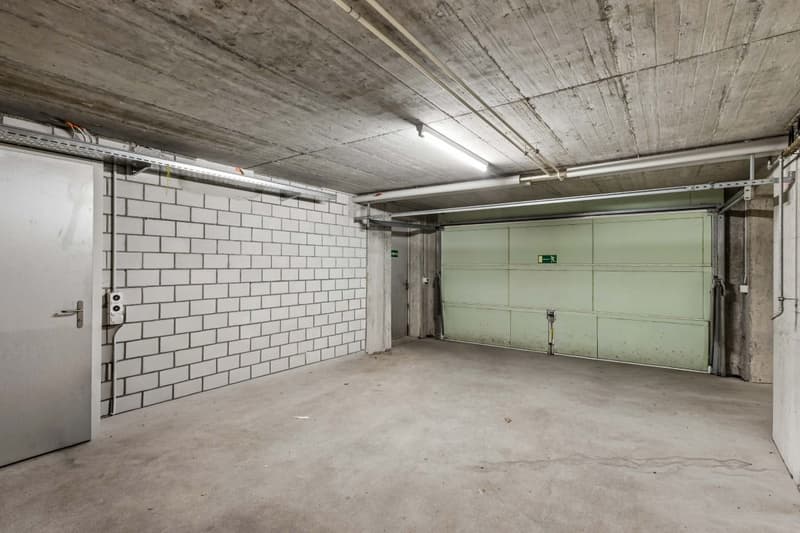Empty garage with white brick wall, concrete floor, and a green garage door.