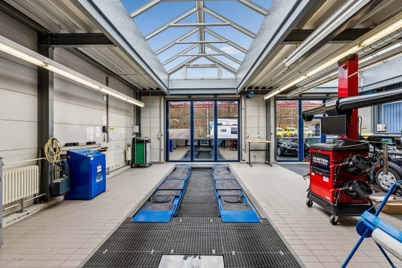 A large garage with a glass roof, a long blue ramp, and various tools and equipment.