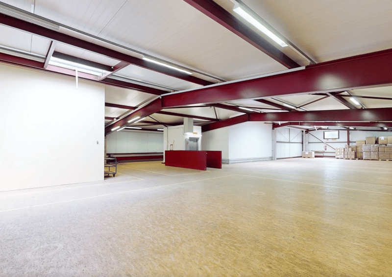Wide open space with wooden floor, white walls, high ceiling with red trusses and white lighting.