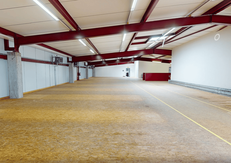 Empty warehouse with yellow floor, red structural beams, high ceiling, white walls, metal partitions, and ceiling lights.
