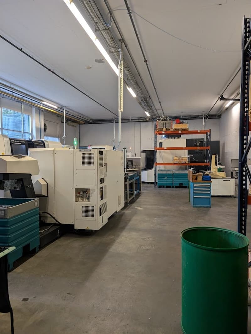 Indoor facility with industrial machines, white walls, grey floor, green bucket, office equipment.