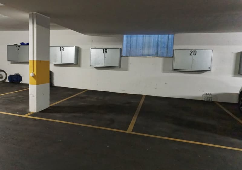 underground parking area with numbered parking spaces, white walls, yellow markings, and a small window