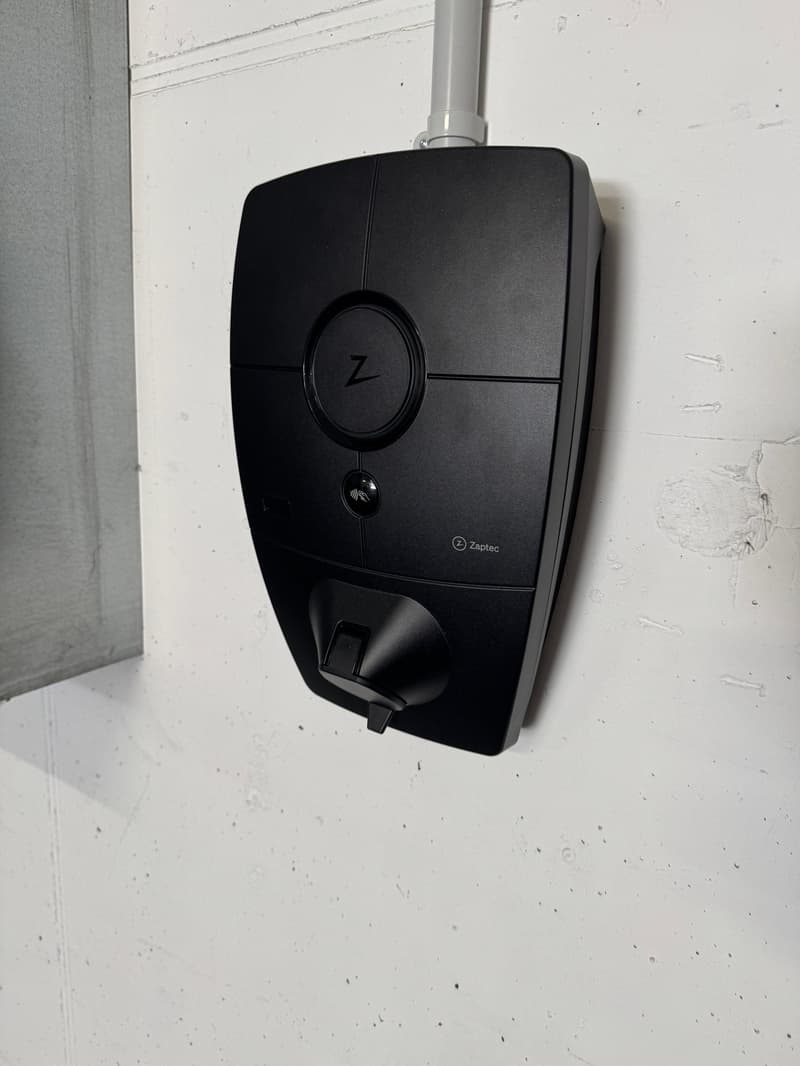 Black electric vehicle charger mounted on white wall, branded Zaptec