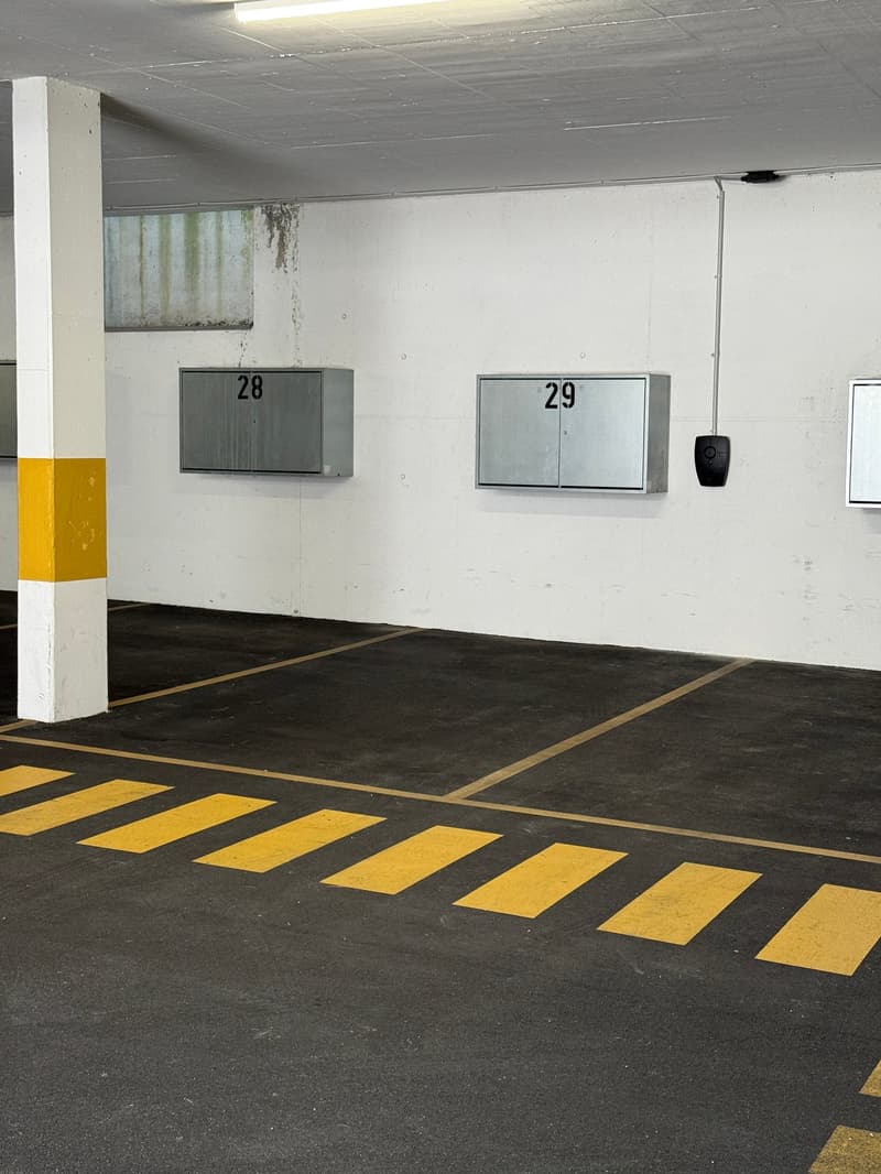 concrete floor, yellow markings, two numbered storage boxes, white walls, ceiling light, column