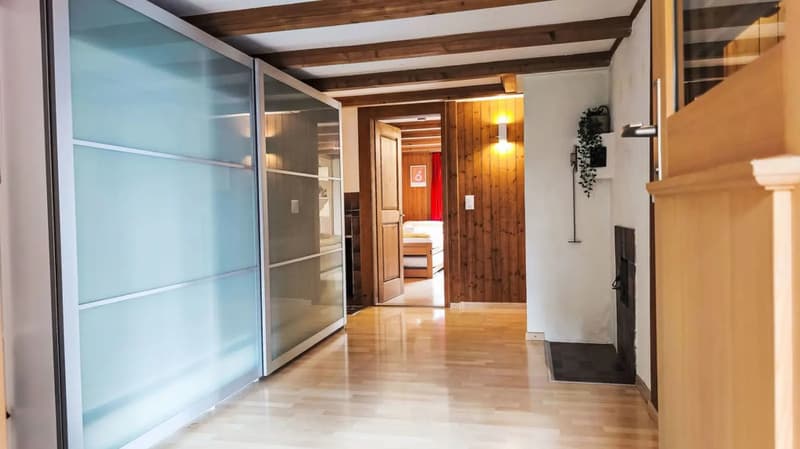 The image shows the interior of a room with a wooden ceiling and walls, hardwood floors, and a glass sliding door. There is a fireplace visible in the background, and the room appears to be part of a larger living space or apartment.