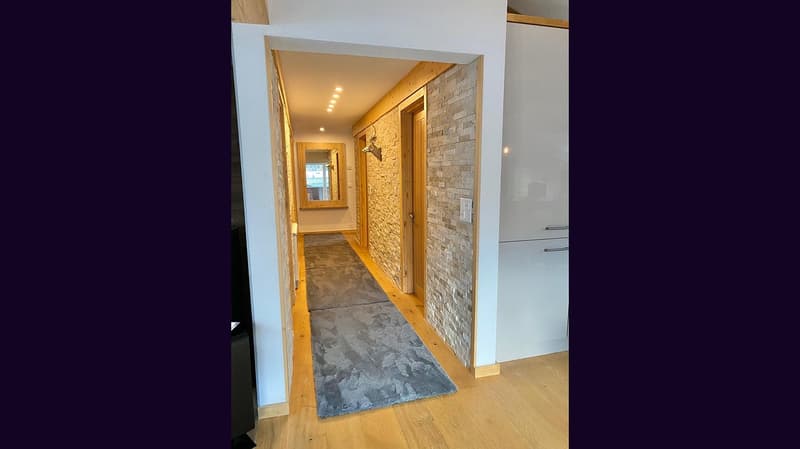 Wide hallway, brick wall, wooden floors, large carpet, mirror
