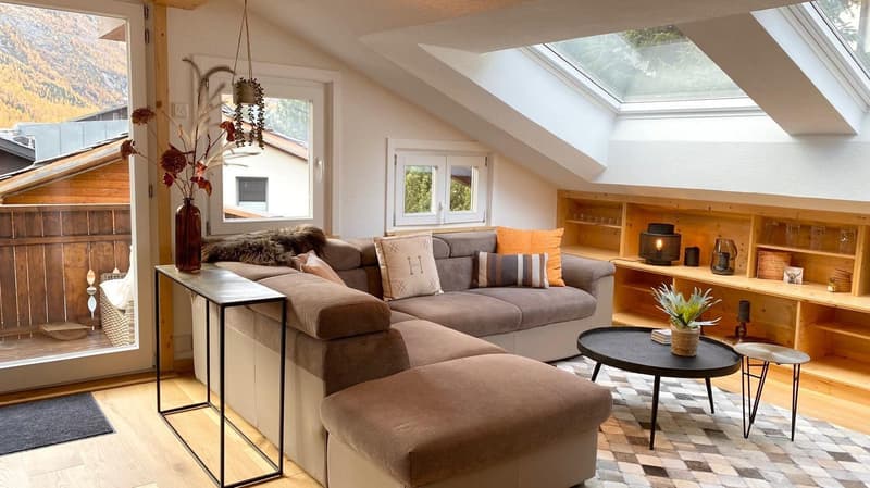 L-shaped couch, coffee table, hanging plant, shelves, wooden floor, balcony, mountain view