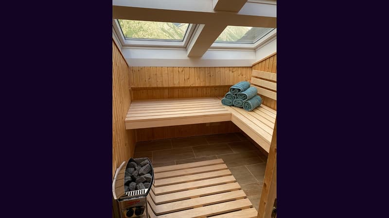 Sauna room with wooden walls, wooden benches, and green towels, wooden flooring, two skylights