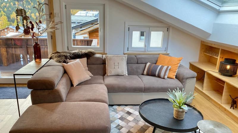 section of living room with L-shaped sofa, window with balcony, carpet, table with plant