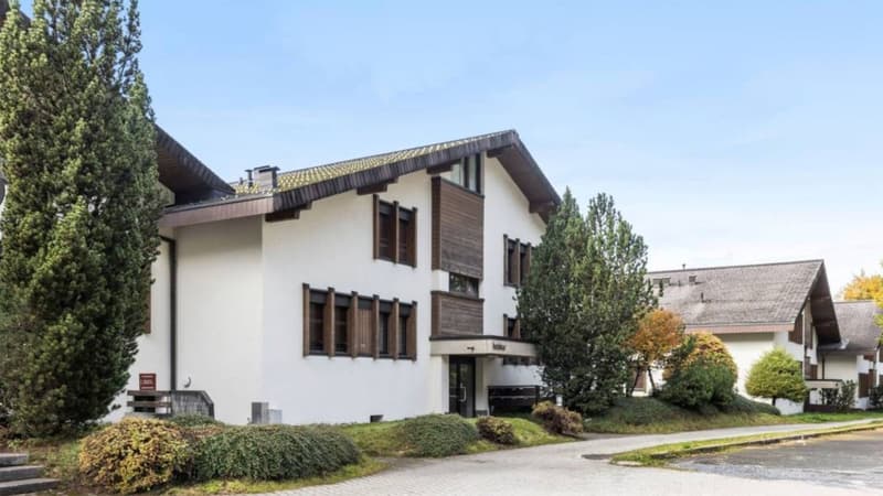 2 story house, white exterior, brown wooden accents, multiple windows, driveway, trees, shrubs