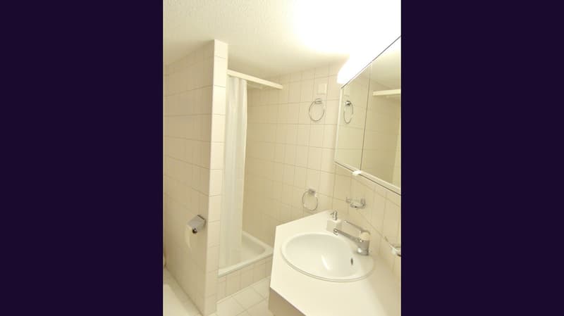Bathroom with white tiles, shower, sink, mirror, and towel rack