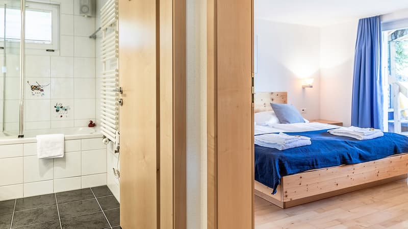 Bathroom with bathtub and shower, bedroom with bed and nightstand