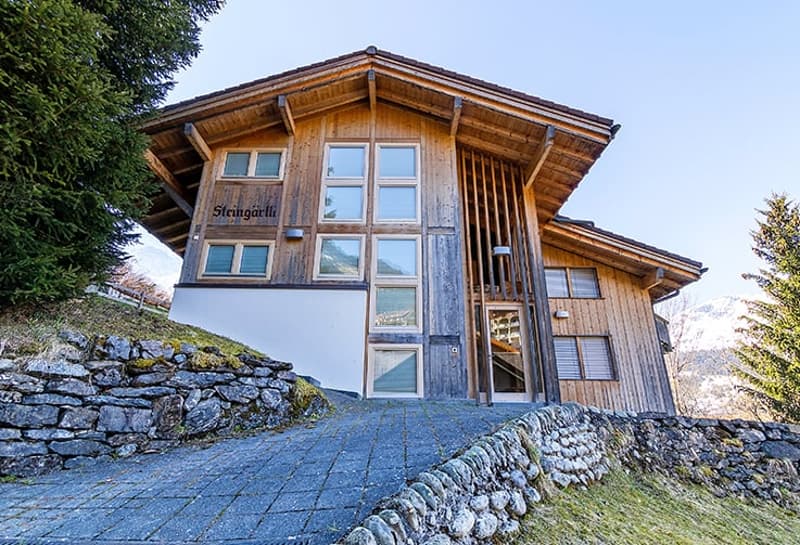 wooden exterior, large windows, stone wall, paved driveway, mountain view