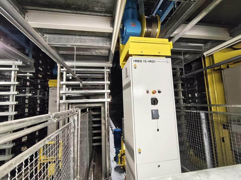 Industrial facility with metal shelving, yellow and blue machinery, control panel, and metal railings.