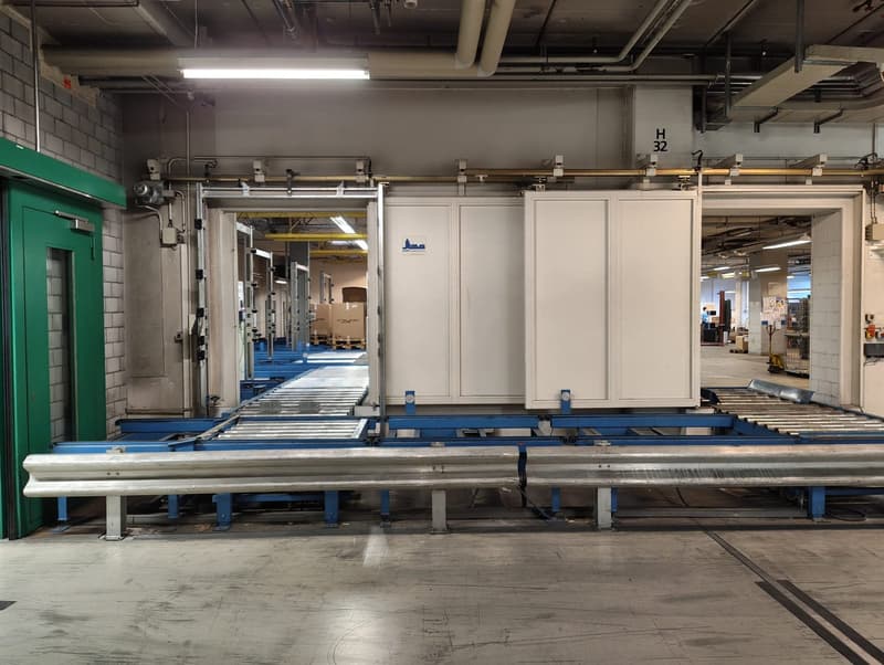 Industrial facility with a conveyor belt system, large white storage units, and a green door.