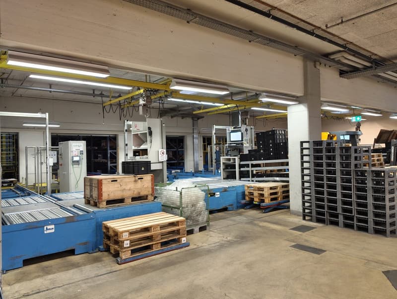 large warehouse with multiple machines, conveyor belts, wooden and plastic pallets, storage boxes, and equipment