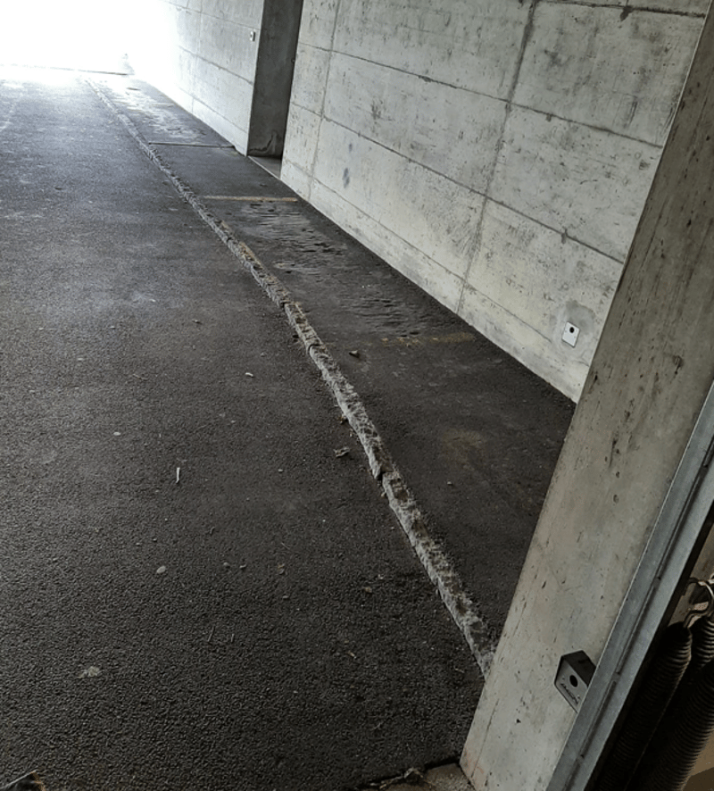 An empty concrete garage with a grey parking area and concrete walls. There is an access point with a white electrical socket