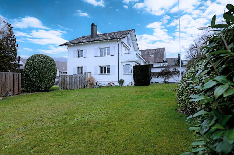 Detached house, brick, white exterior, 3 stories, chimney, fenced garden, multiple windows, bushes, trees