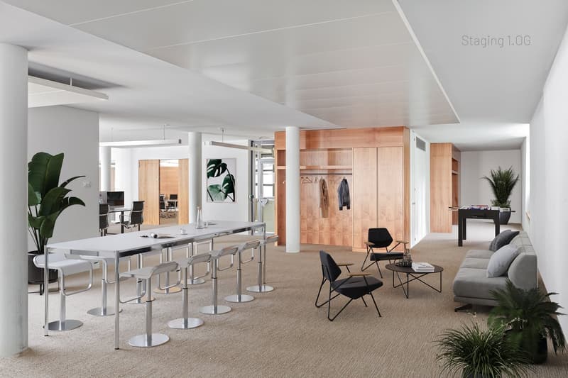 large white desk with metal stools, two modern black armchairs, small coffee table, grey sofa with pillows, black bar cart with foosballs, office furniture