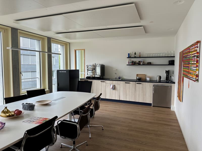 wooden floor, large windows, long table, chairs, modern kitchen, refrigerator, coffee machine, shelves with glassware