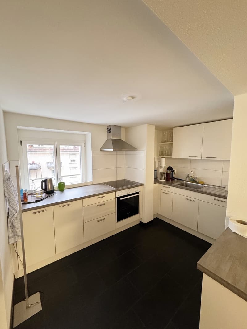 fully equipped kitchen, stainless steel appliances, white cabinets, dark floor tiles, window with city view