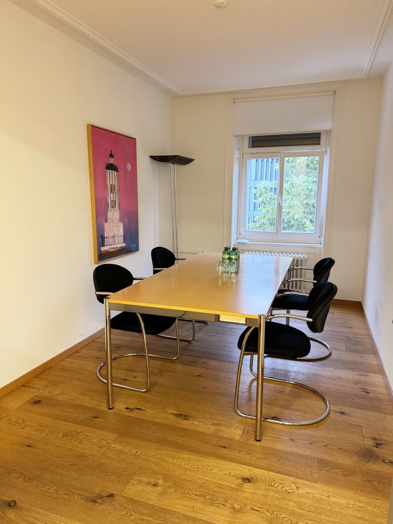 modern wooden floor, white walls, large window, round long table, black modern chairs, painting on wall, metal lamp