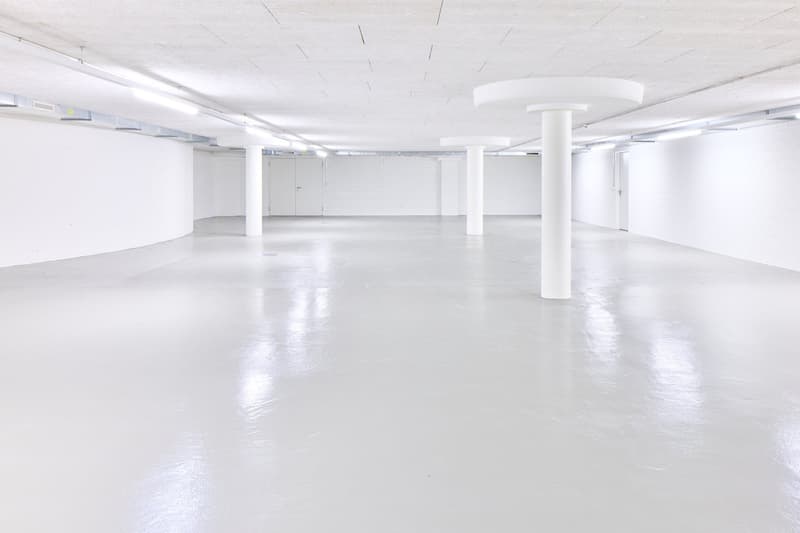 Large open-plan commercial space with white walls, concrete floors, and recessed lighting. The space appears to be empty and ready for use, with several white columns supporting the ceiling.