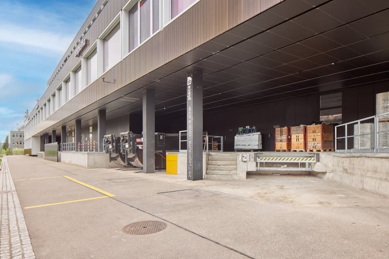 Large industrial building with loading docks, parking spaces, and storage containers outside
