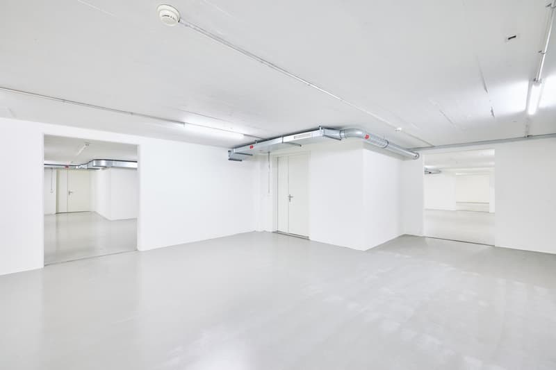 Large open commercial space with white walls, concrete floor, and overhead ventilation ducts. The space appears to be empty and ready for customization or use.