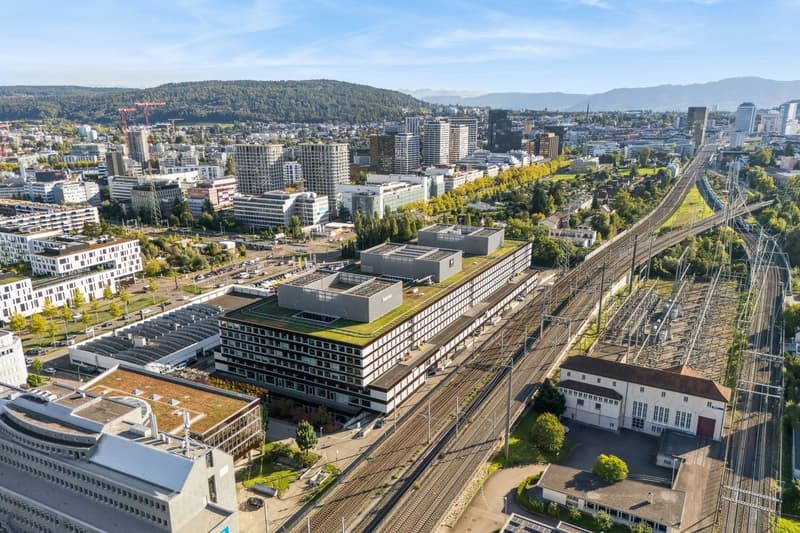 Aerial view of a city with modern buildings, trees, and a railway with a small building.
