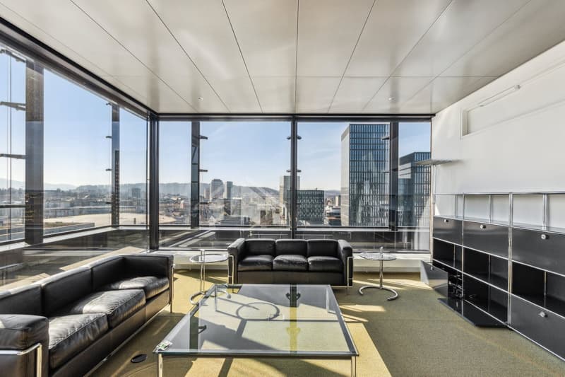 Spacious living room with floor-to-ceiling windows offering a panoramic view of the city skyline, black leather sofas, glass coffee table, and built-in storage units