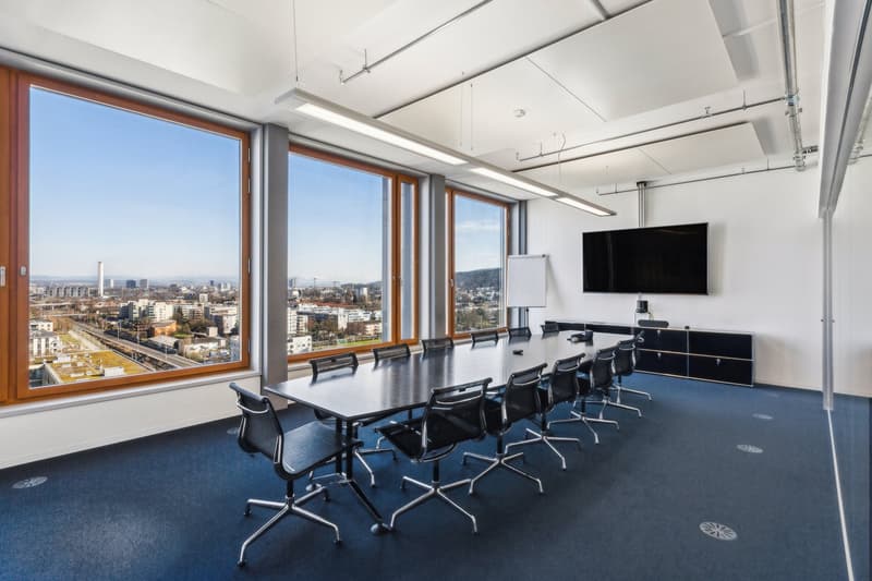 Long conference table, black chairs, white walls, large windows with city view, TV, whiteboard
