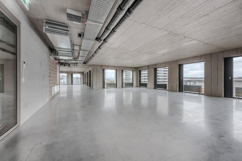 Empty room with large windows, concrete floor, metal pipes on ceiling