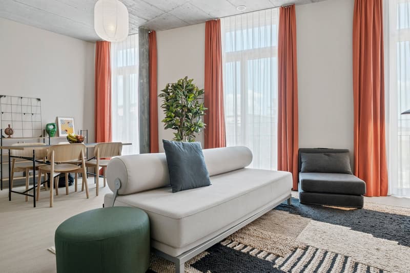 open-plan room with a couch, chair, ottoman, and a desk with dining chairs, large windows, and a view