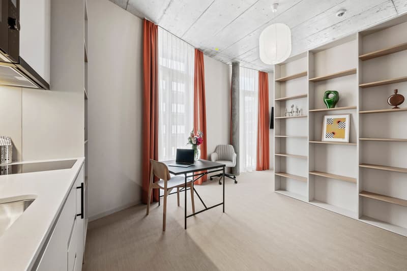 Modern kitchen with desk and chair, white cabinets, double sink, large windows with curtains, built-in shelves with decorative items