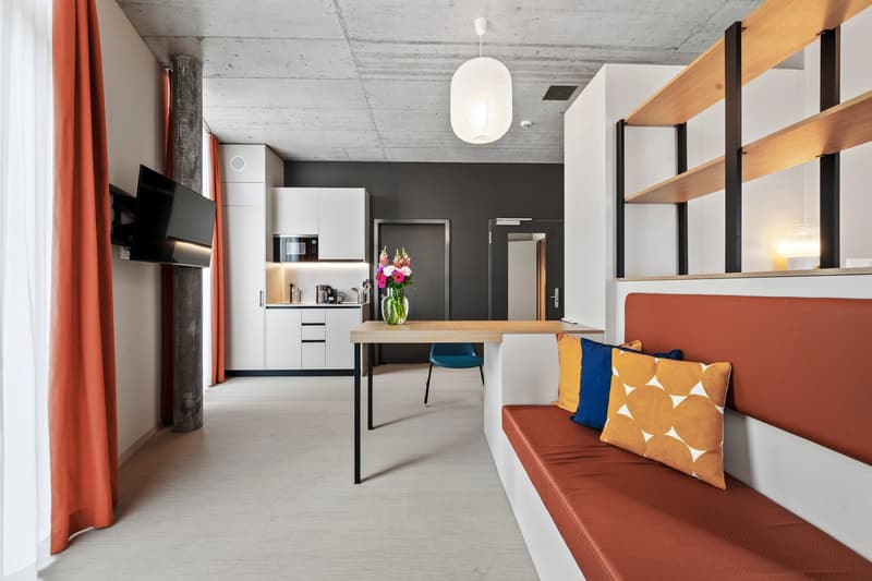 modern room, dining area, white cabinetry, concrete wall, mounted tv, flowers, cushions