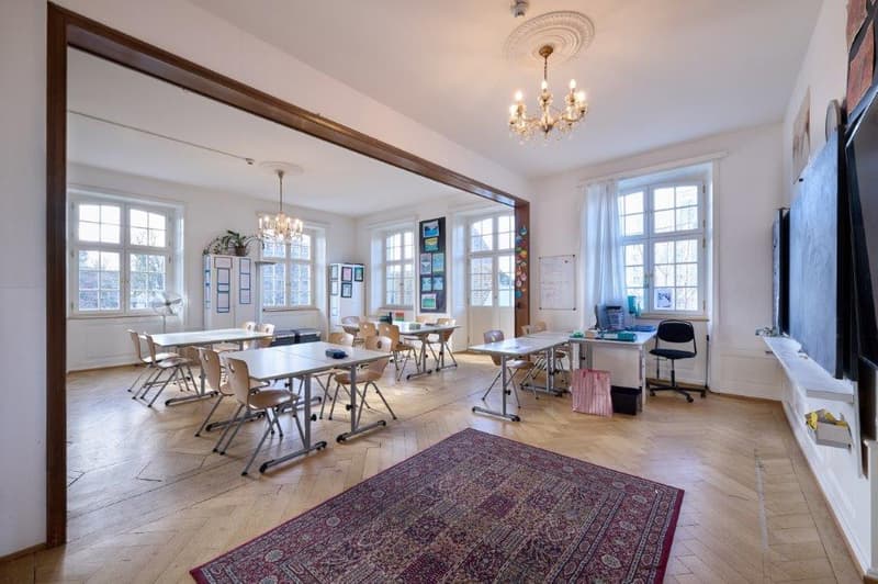 classroom with tables, chairs, large mirror, chandelier, windows, rug, chalkboard, shelves