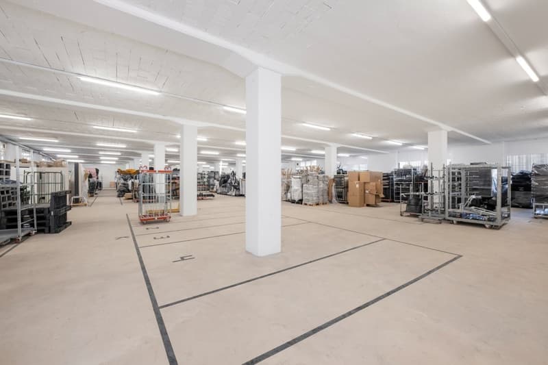 large open space, white walls, high ceiling, fluorescent lighting, storage boxes, shelves, trolleys